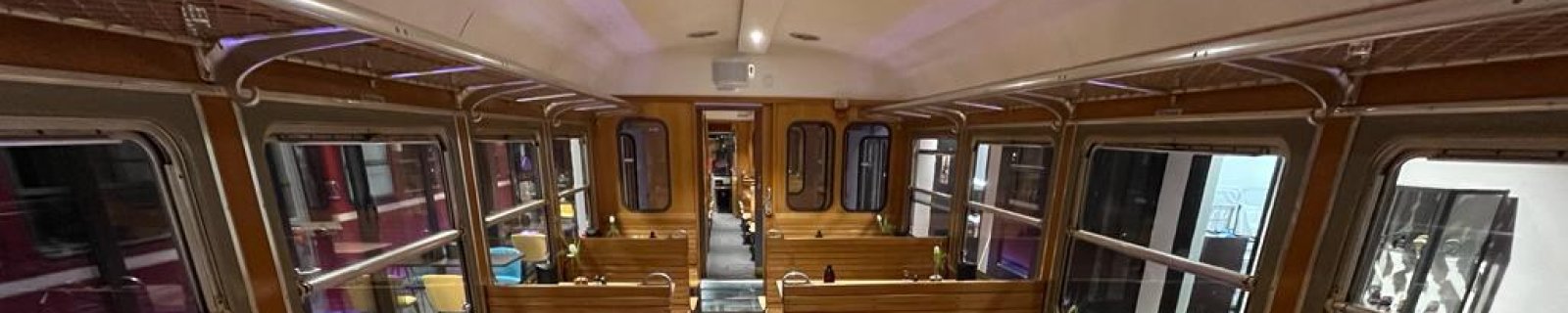 Speisewagen im Zug mit Holzsitzplätzen und Tischen, dekoriert mit kleinen Blumenvasen.