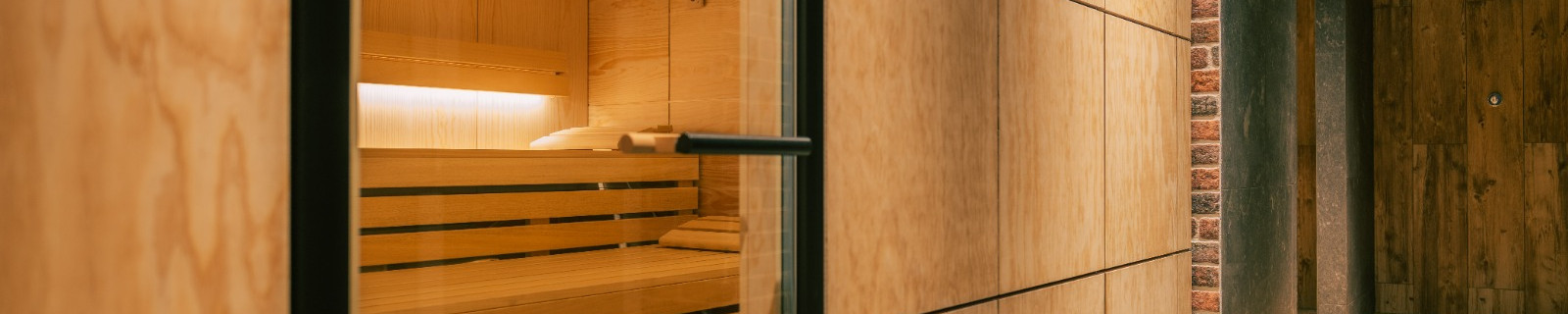 Sauna mit Holzverkleidung und Glastür, daneben eine Ziegelwand.