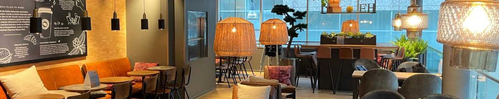 Innenraum eines modernen Cafés mit Holzboden, verschiedenen Sitzbereichen und dekorativem Licht.