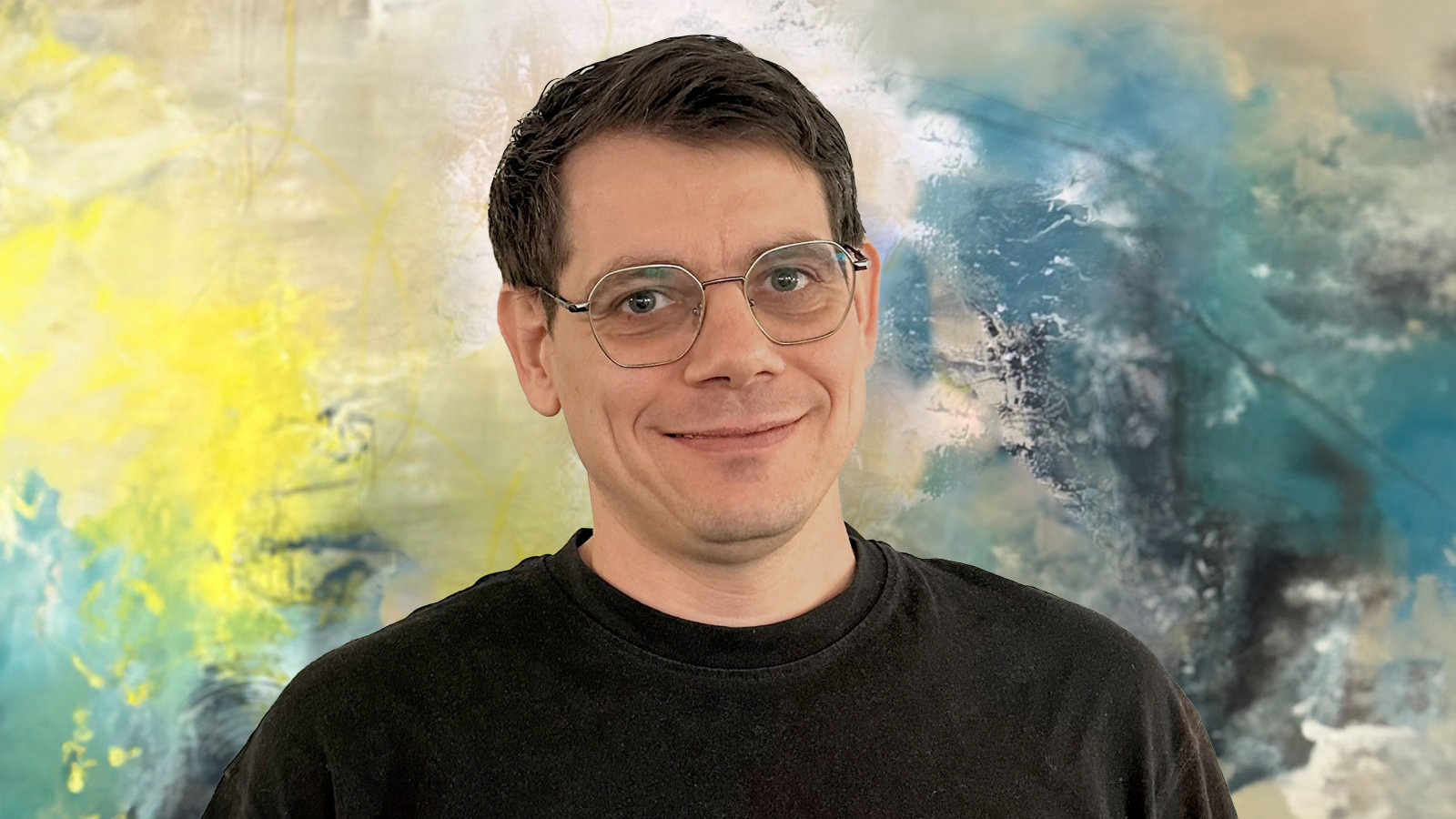 Mann mit Brille lächelt vor einem abstrakten, bunten Hintergrund.