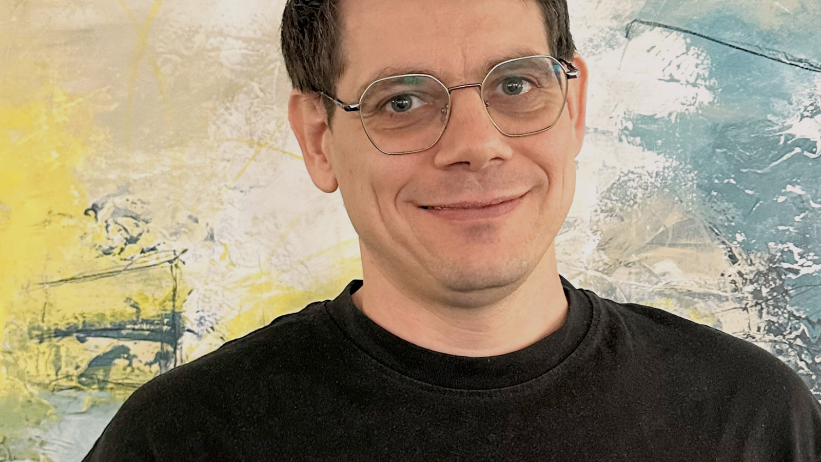 Mann mit Brille vor einem abstrakten, künstlerischen Hintergrund.
