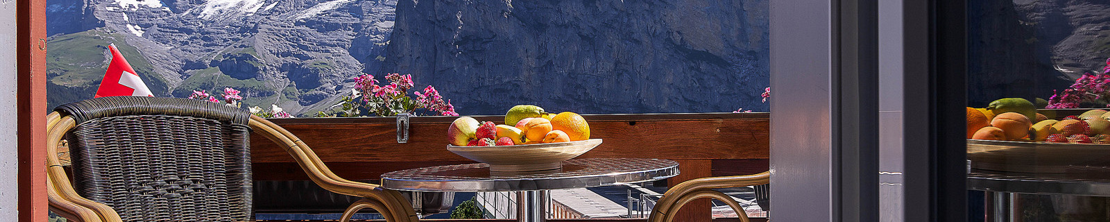 Balkon mit Stühlen und Tisch, dahinter die schneebedeckten Berge der Schweizer Alpen.