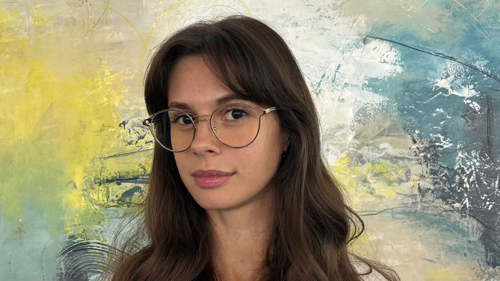 Frau mit langen Haaren und Brille vor einem abstraktem Hintergrund.